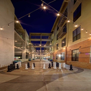 Hero image of an interior courtyard with hanging lights strung between buildings and a life-size chess court